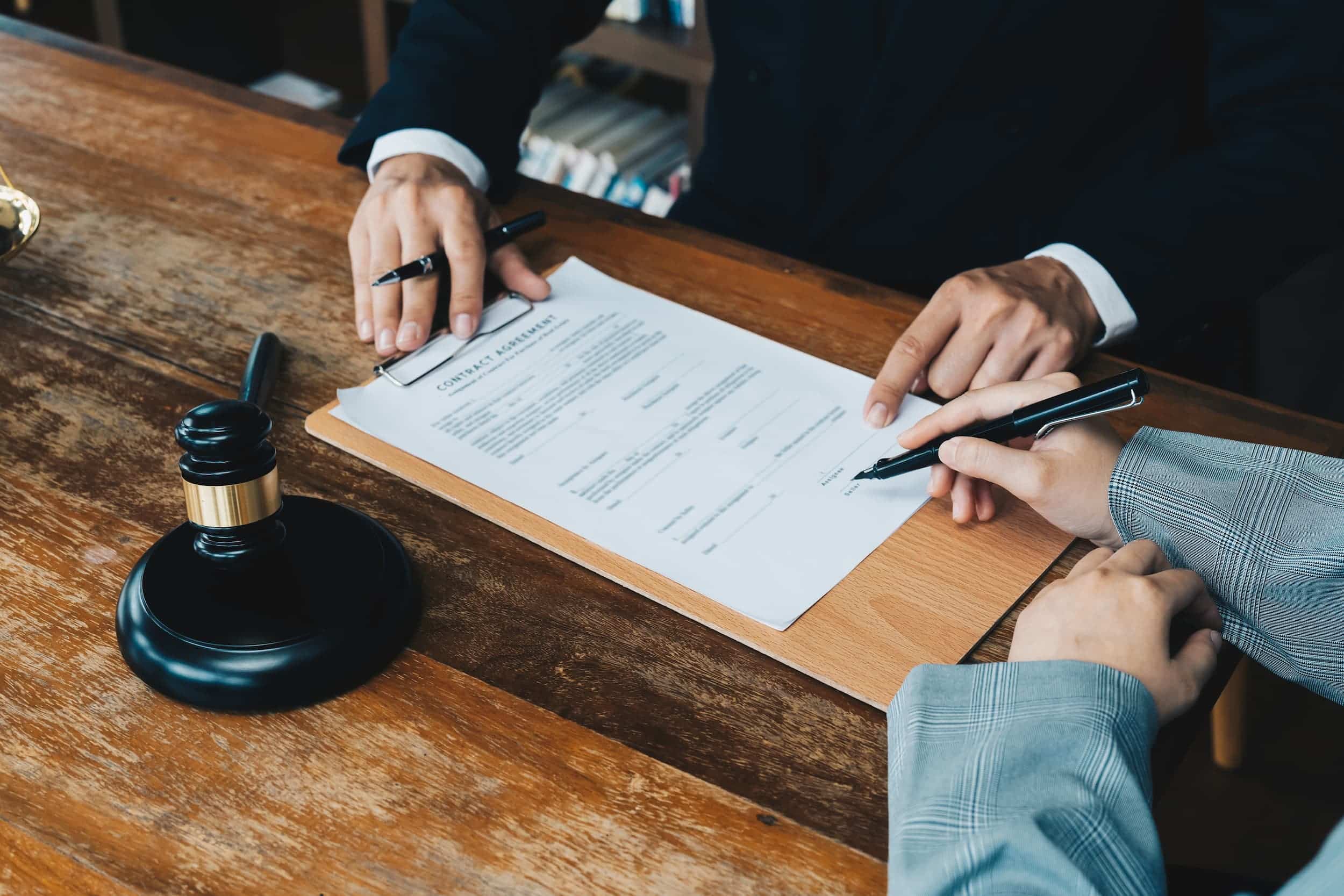 Lawyer and client signing legal contract at office desk.
