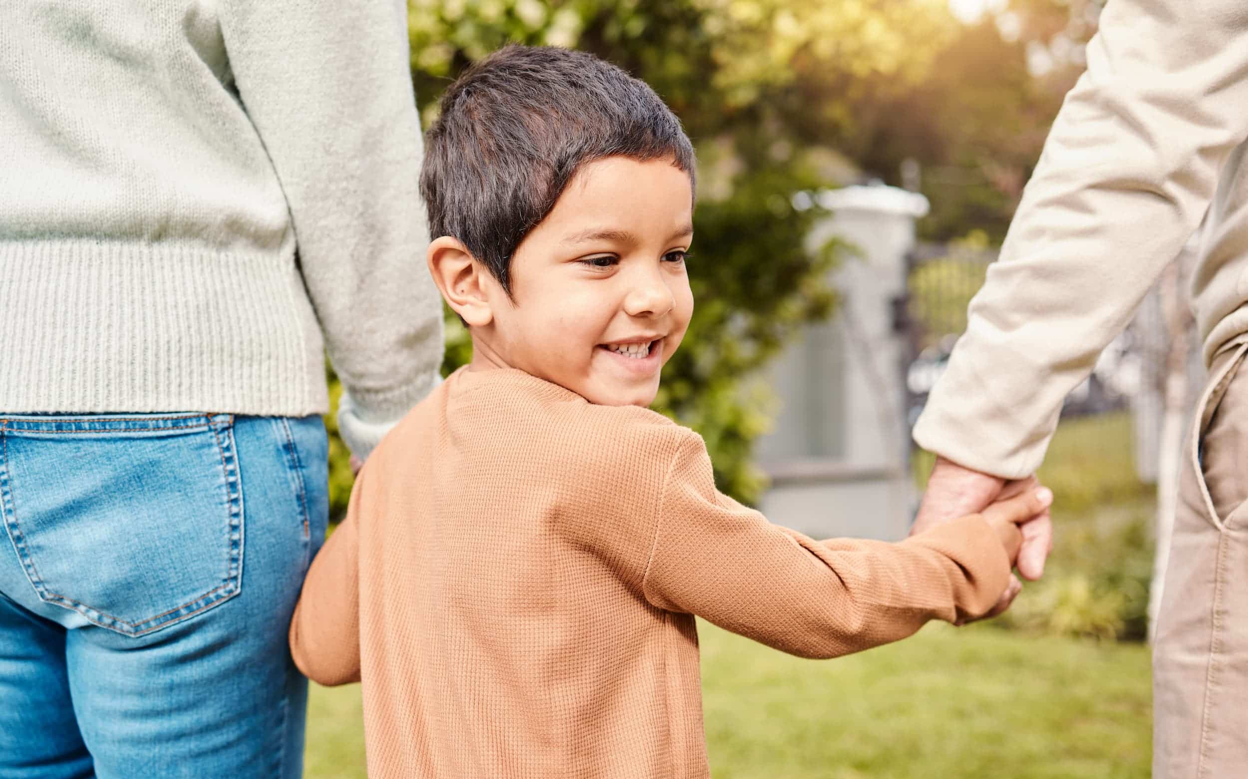Happy child holding hands with parents outdoors in a park.