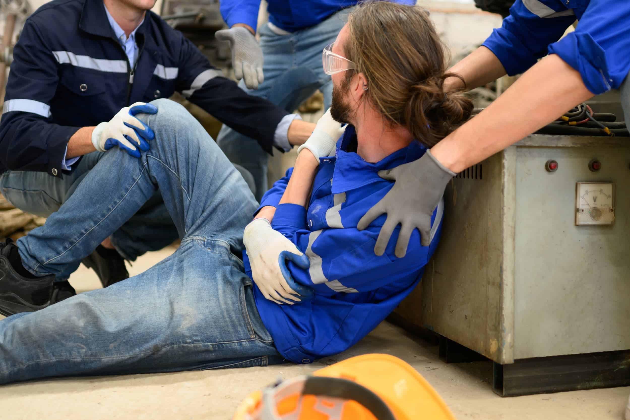 Injured worker being assisted by colleagues in factory setting.