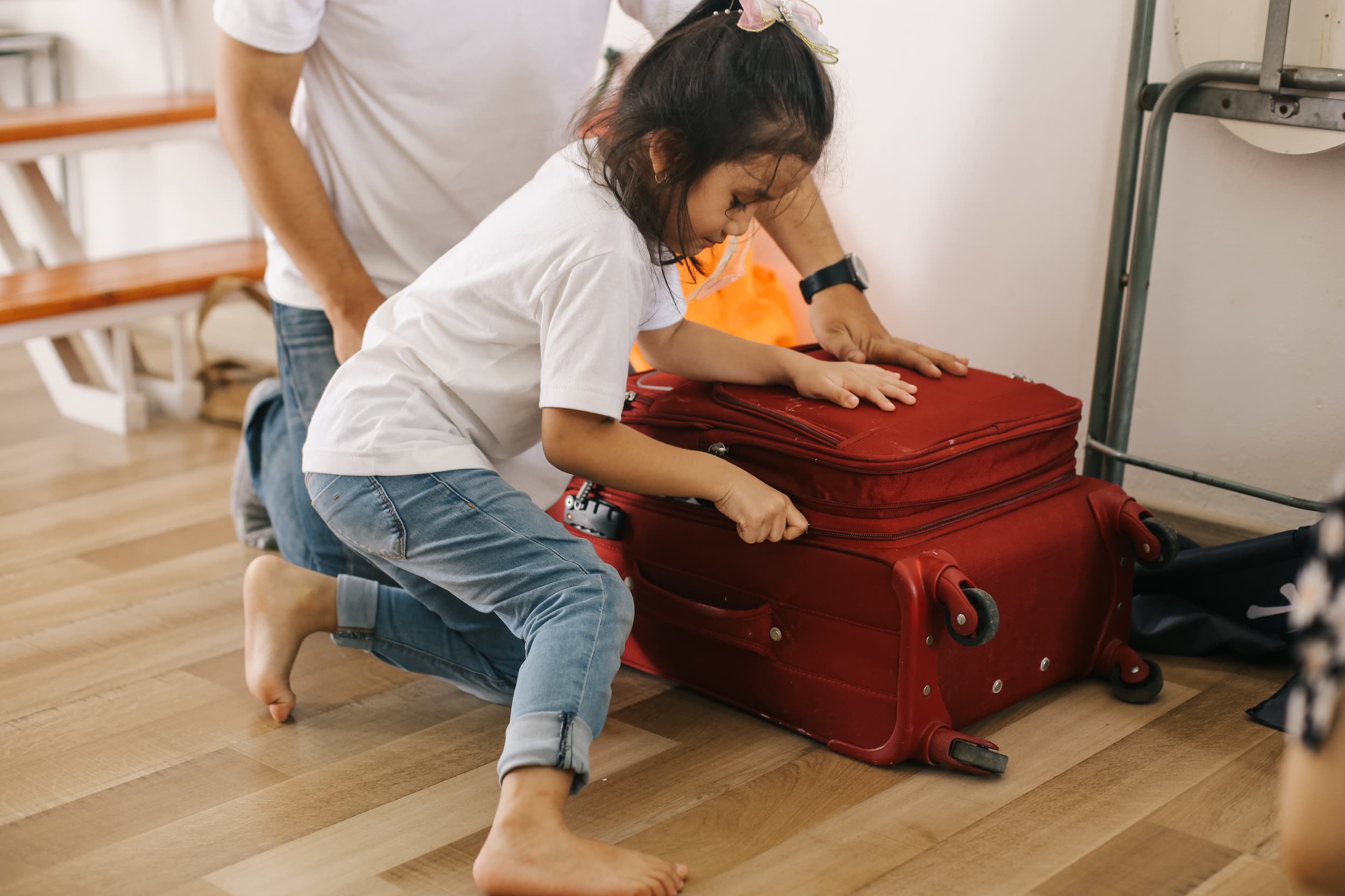 Young girl packing red suitcase with father’s support during move.