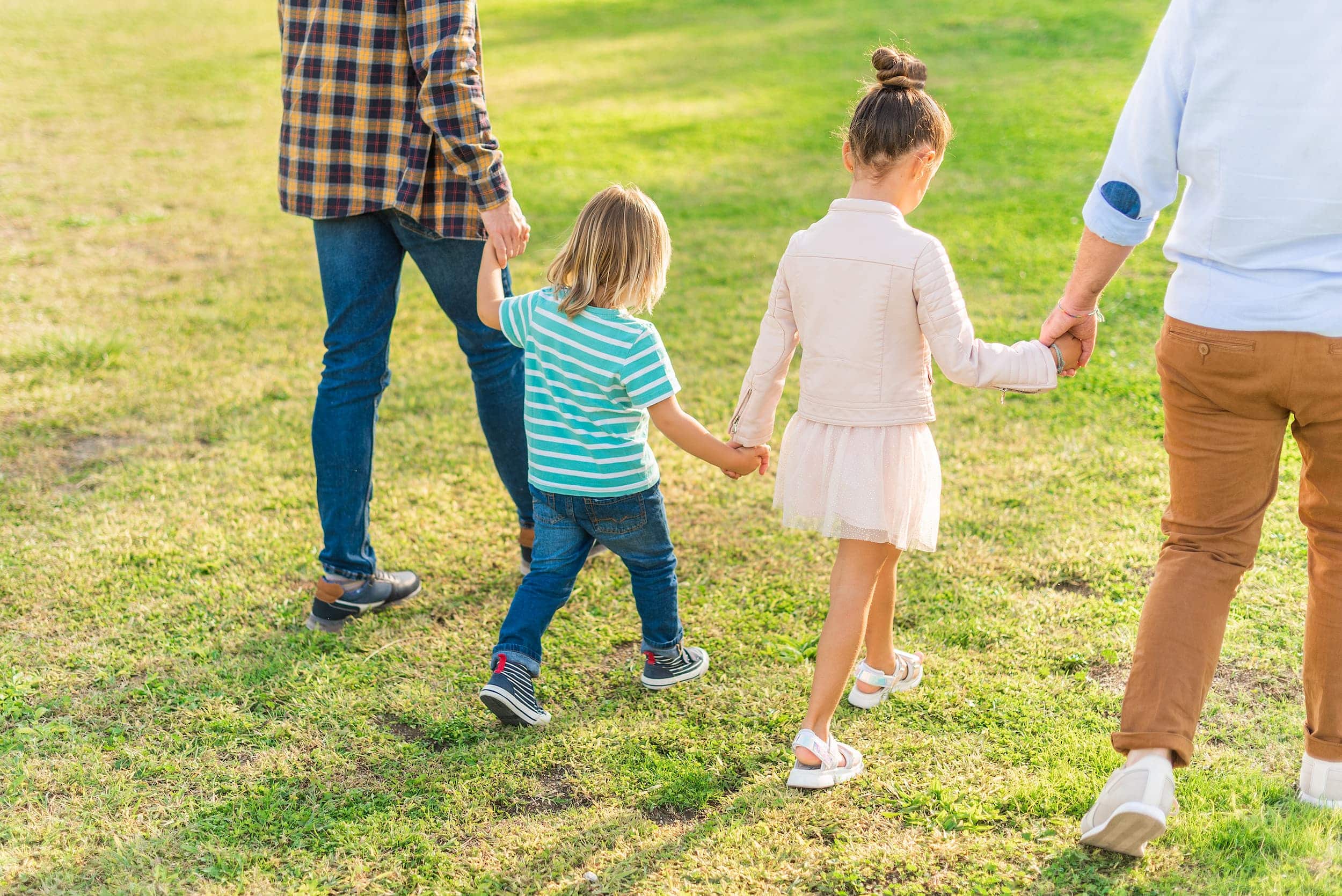 Two children walking hand in hand with their dads in a sunny park.