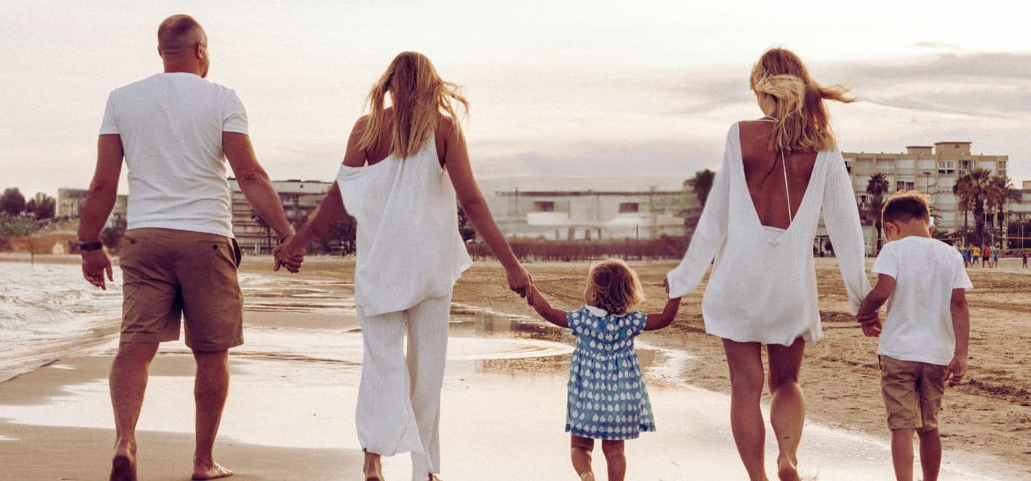 amily holding hands, walking together along beach